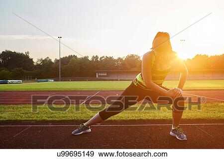 Young female runner stretching on sunlit race track View Large Photo Image Stock Photo - Young female runner stretching on sunlit race track. Fotosearch