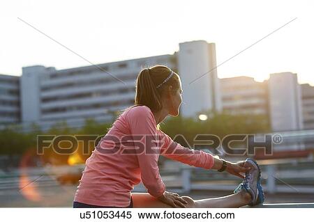 Stock Photography - Young female runner touching toes on rooftop. Fotosearch