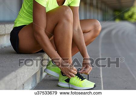 Young female runner tying trainer laces in stadium seating View Large Photo Image Stock Photo - Young female runner tying trainer laces in stadium seating. Fotosearch