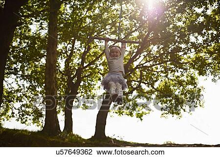 Stock Image - Young girl swinging on tree swing. Fotosearch