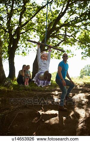 Young girl swinging on tree swing while her family watch View Large Photo Image Stock Photograph - Young girl swinging on tree swing while her family watch. Fotosearch