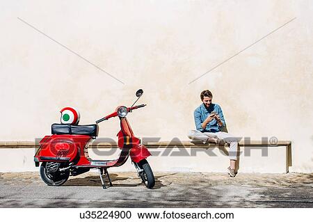 Young male moped rider sitting on bench reading smartphone texts, Florence, Italy View Large Photo Image Stock Image - Young male moped rider sitting on bench reading smartphone texts, Florence, Italy. Fotosearch