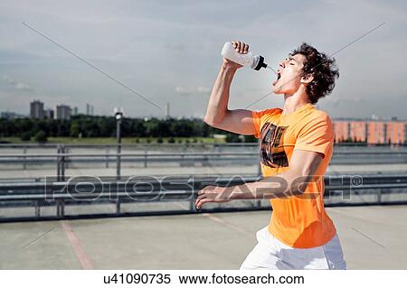 Stock Photography - Young male runner drinking water whilst city running. Fotosearch