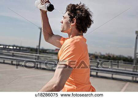 Stock Photography - Young male runner pouring water on his face whilst running in city. Fotosearch