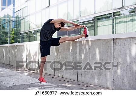 Stock Photo - Young male runner warming up on sidewalk. Fotosearch