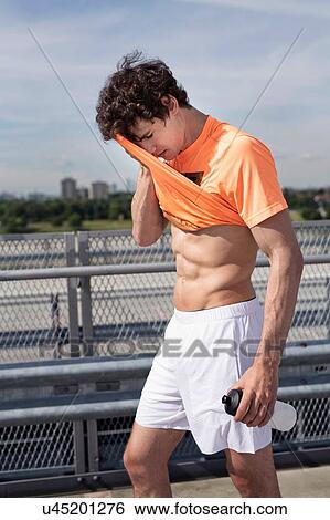Young male runner wiping his brow with tshirt in city View Large Photo Image Stock Photograph - Young male runner wiping his brow with tshirt in city. Fotosearch