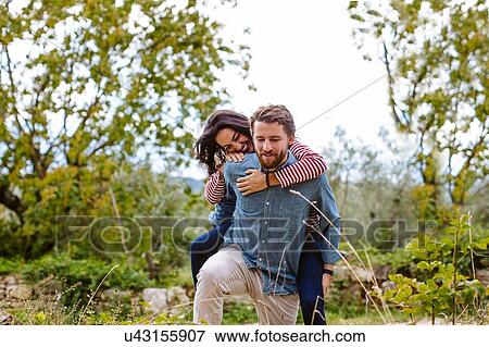 Stock Photo - Young man giving girlfriend a piggy back in olive grove, Florence, Italy. Fotosearch