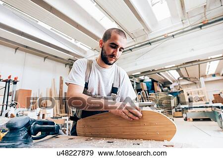 Young man in carpentry workshop looking down sanding skateboard View Large Photo Image Stock Photo - Young man in carpentry workshop looking down sanding skateboard. Fotosearch