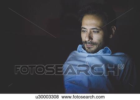 Young man leaning back looking down illuminated by laptop computer screen View Large Photo Image Stock Photo - Young man leaning back looking down illuminated by laptop computer screen. Fotosearch