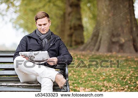Young man reading newspaper on park bench View Large Photo Image Stock Image - Young man reading newspaper on park bench. Fotosearch
