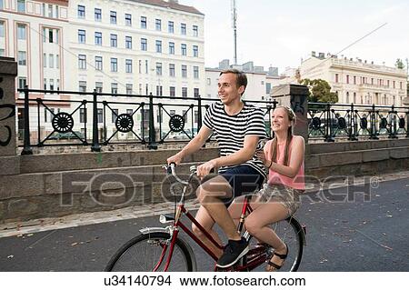 Picture - Young man riding bicycle with young woman sitting on back smiling. Fotosearch