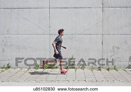 Young man running along on urban sidewalk View Large Photo Image Stock Image - Young man running along on urban sidewalk. Fotosearch