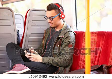 Young man sitting on train, using smartphone, wearing headphones View Large Photo Image Stock Image - Young man sitting on train, using smartphone, wearing headphones. Fotosearch