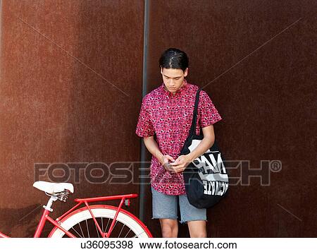 Stock Photo - Young man standing beside bicycle. Fotosearch