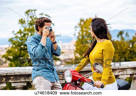Stock Photo - Young man taking photographs of girlfriend in front of view from San Miniato church, Florence, Italy. Fotosearch