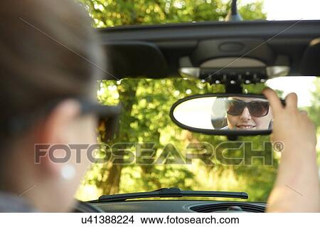 Picture - Young woman adjusting mirror in convertible car. Fotosearch