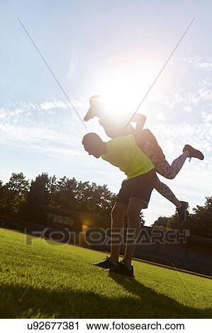 Stock Image - Young woman and man fooling around whilst training in park. Fotosearch