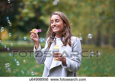 Stock Photograph - Young woman blowing bubbles in autumn park. Fotosearch