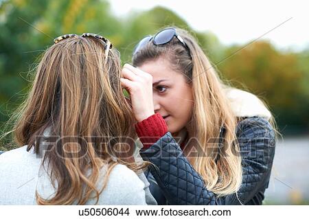Picture - Young woman brushing hair from friend's face, rear view. Fotosearch