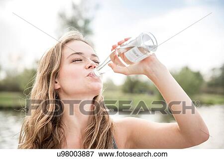 Stock Photo - Young woman drinking water from bottle, outdoors. Fotosearch