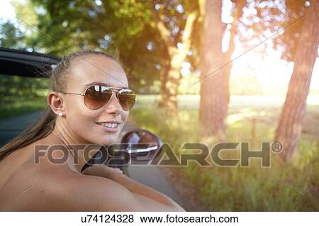 Young woman driving convertible looking over her shoulder View Large Photo Image Stock Photo - Young woman driving convertible looking over her shoulder. Fotosearch