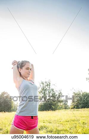 Stock Photo - Young woman exercising, stretching, in field. Fotosearch
