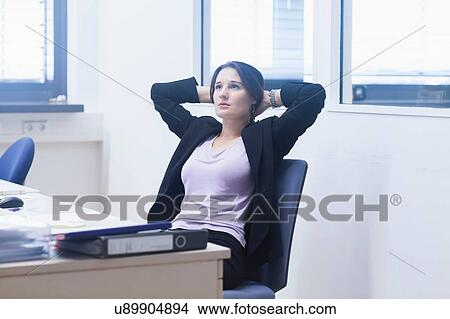 Young woman in office leaning back in chair hands behind head looking away View Large Photo Image Picture - Young woman in office leaning back in chair hands behind head looking away. Fotosearch