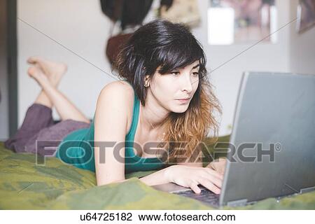 Young woman lying on front on bed using laptop computer View Large Photo Image Stock Image - Young woman lying on front on bed using laptop computer. Fotosearch