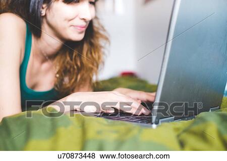 Young woman lying on front on bed using laptop computer smiling, differential focus View Large Photo Image Stock Photo - Young woman lying on front on bed using laptop computer smiling, differential focus. Fotosearch