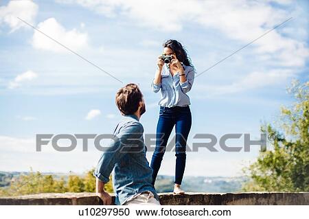 Stock Image - Young woman photographing boyfriend from wall in Florence hills, Italy. Fotosearch