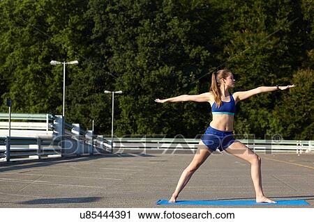 Stock Image - Young woman practicing yoga in urban parking lot. Fotosearch