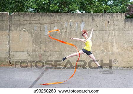 Stock Image - Young woman practising ribbon dance on court. Fotosearch