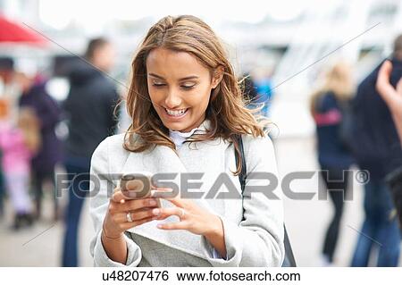 Stock Photograph - Young woman reading smartphone texts on city street. Fotosearch