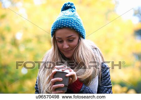 Young woman removing lid from takeaway coffee in park View Large Photo Image Stock Photo - Young woman removing lid from takeaway coffee in park. Fotosearch