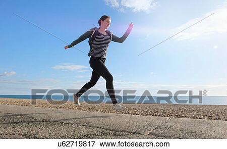 Young woman running along path on shingle beach View Large Photo Image Stock Photo - Young woman running along path on shingle beach. Fotosearch