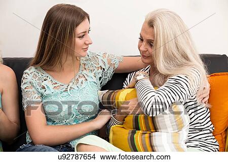 Young woman sitting on sofa comforting mature woman hugging cushion View Large Photo Image Picture - Young woman sitting on sofa comforting mature woman hugging cushion. Fotosearch