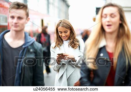 Stock Photography - Young woman walking outdoors, using smartphone. Fotosearch