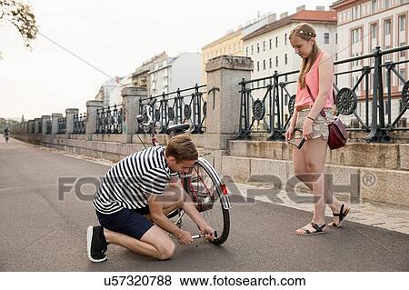 Young woman watching young man kneeling inflating bicycle tyre View Large Photo Image Stock Photo - Young woman watching young man kneeling inflating bicycle tyre. Fotosearch