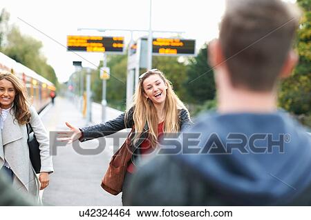 Picture - Young woman, with arms open, greeting young man, at railway station. Fotosearch