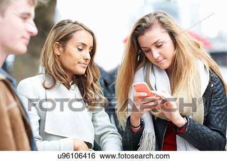 Young woman with friends reading taking smartphone texts on street View Large Photo Image Stock Photograph - Young woman with friends reading taking smartphone texts on street. Fotosearch