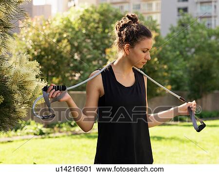 Stock Image - Young woman with resistance band over shoulder. Fotosearch