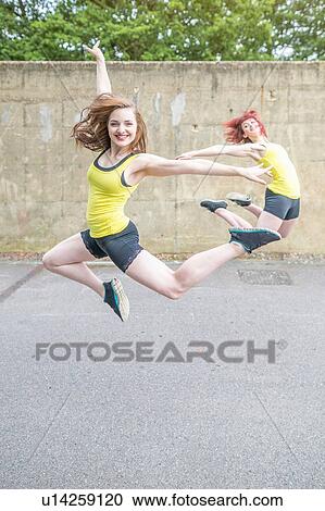 Stock Image - Young women jumping in front of concrete wall. Fotosearch