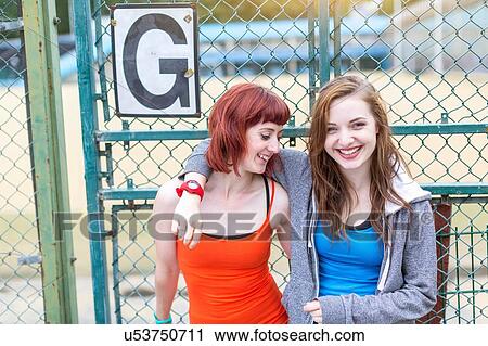 Stock Image - Young women standing beside sports ground, London, UK. Fotosearch