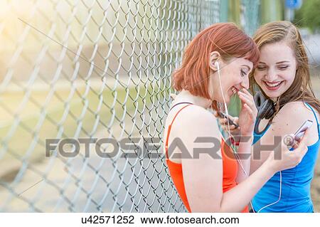 Young women using smartphone beside fence, London, UK View Large Photo Image Stock Image - Young women using smartphone beside fence, London, UK. Fotosearch