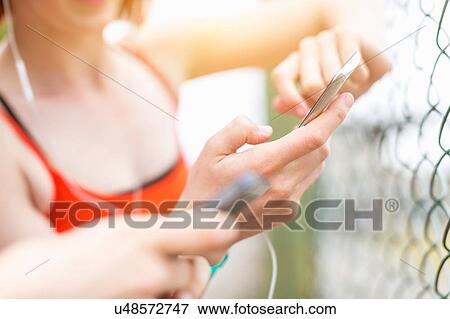 Stock Photo - Young women using smartphone beside fence. Fotosearch