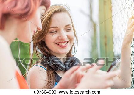 Young women using smartphone beside fence View Large Photo Image Stock Photo - Young women using smartphone beside fence. Fotosearch