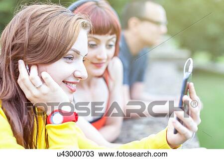 Young women using smartphone, leaning on low wall View Large Photo Image Stock Image - Young women using smartphone, leaning on low wall. Fotosearch