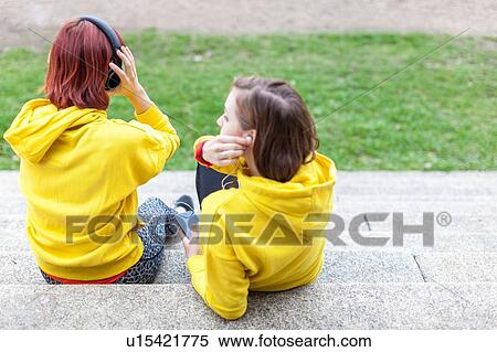 Stock Photography - Young women with earphones resting on steps. Fotosearch