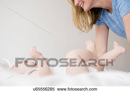 Baby girl (12-17 months) lying down on bed and mother leaning over View Large Photo Image Stock Photography - Baby girl (12-17 months) lying down on bed and mother leaning over. Fotosearch