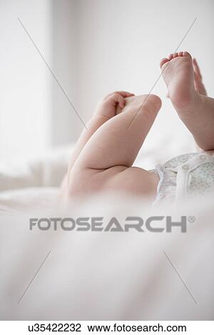 Stock Image - Baby girl (12-17 months) lying down with hands on feet. Fotosearch